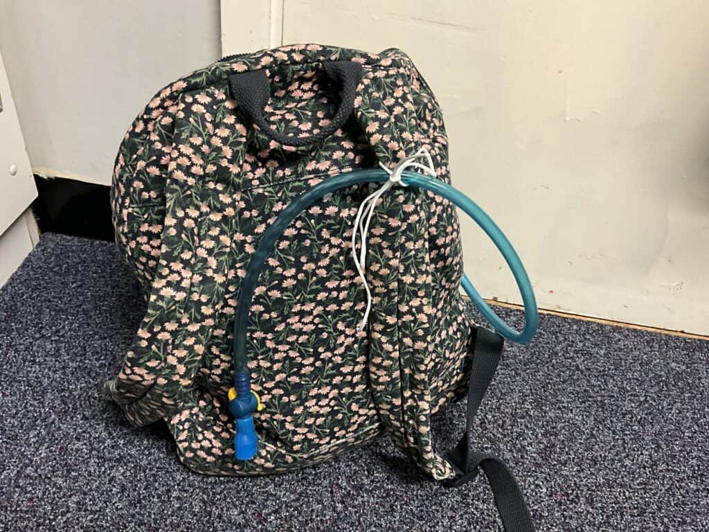 Backpack with hydration bladder bite valve secured to the front using string